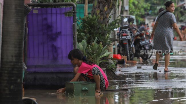 Seorang anak membersihkan halaman depan rumahnya dari sisa - sisa banjir di Perumahan Villa Jatirasa, Kota Bekasi, Jawa Barat, Minggu (25/10). [Suara.com/Alfian Winanto]