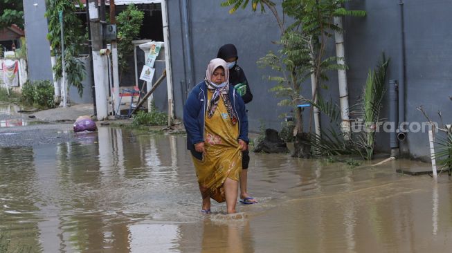 Warga melintas di area jalan yang masih tergenang banjir di Perumahan Villa Jatirasa, Kota Bekasi, Jawa Barat, Minggu (25/10). [Suara.com/Alfian Winanto]