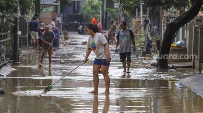 Para warga membersihkan rumahnya dari lumpur sisa banjir di Perumahan Villa Jatirasa, Kota Bekasi, Jawa Barat, Minggu (25/10). [Suara.com/Alfian Winanto]