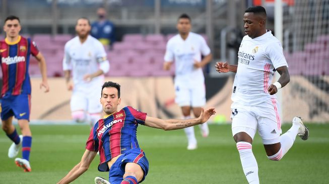 Penyerang Real Madrid, Vinicius Junior (kanan), menantang gelandang Barcelona Sergio Busquets dalam  pertandingan sepak bola Liga Spanyol antara Barcelona melawan Real Madrid di stadion Camp Nou, Barcelona, Spanyol, Sabtu (24/10). [LLUIS GENE / AFP]