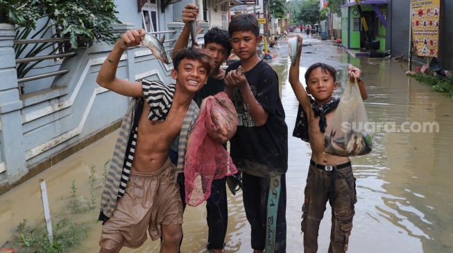 Anak - anak mencari ikan yanh tersapu banjir di Perumahan Villa Jatirasa, Kota Bekasi, Jawa Barat, Minggu (25/10). [Suara.com/Alfian Winanto]