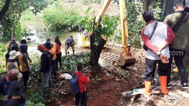 BPBD Kota Bogor mengerahkan alat berat ekskavator untuk melakukan penggalian gorong-gorong yang menyebabkan saluran air tersumbat dan berdampak puluhan rumah di Perumahan Griya Cimanggu Indah terendam banjir, Senin (26/10/2020). [Suara.com/Andi Ahmad Sulaendi]