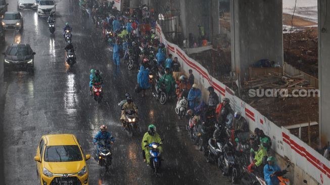 Puluhan pengendara motor berteduh dibawah proyek layang LRT di Jalan Gatot Subroto, Jakarta, Senin (26/10). [Suara.com/Alfian Winanto]