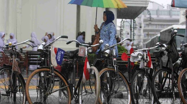 Ilustrasi - Seorang ASN perempuan menggunakan payung saat hujan. [Foto: Ayobandung.com]