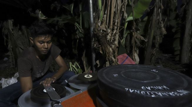 Teknisi mempersiapkan film 35mm untuk pemutaran film layar tancap di kawasan Serua, Bojongsari, Depok, Jawa Barat, Sabtu (19/9/2020). [Suara.com/Angga Budhiyanto] 