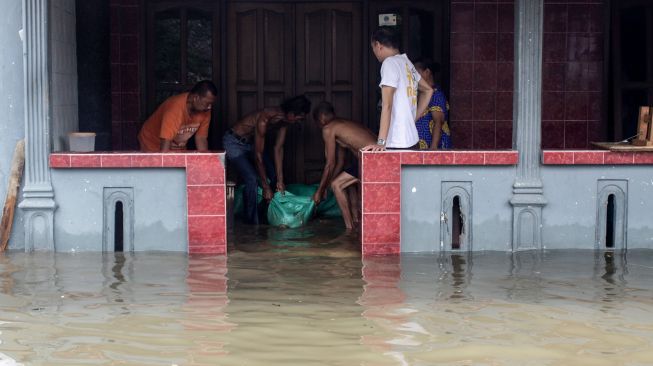 Warga menutup celah pintu rumahnya dengan karung berisi pasir saat banjir merendam kawasan jalan raya Gempol, Pasuruan, Jawa Timur, Senin (2/11/2020). [ANTARA FOTO/Umarul Faruq]