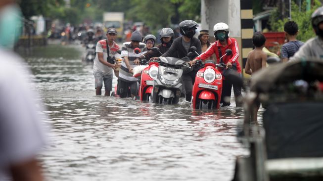 Pengendara sepeda motor mendorong kendaraannya saat menerobos jalan yang tergenang banjir di kawasan jalan raya Gempol, Pasuruan, Jawa Timur, Senin (2/11/2020). [ANTARA FOTO/Umarul Faruq]