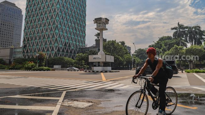 Seorang pesepeda melintas disekitar area Tugu Jam Thamrin di Jl. MH. Thamrin, Jakarta Pusat, Minggu (8/11). [Suara.com/Alfian Winanto]