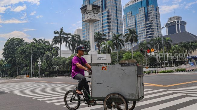 Pedagang melintas disekitar area Tugu Jam Thamrin di Jl. MH. Thamrin, Jakarta Pusat, Minggu (8/11). [Suara.com/Alfian Winanto]