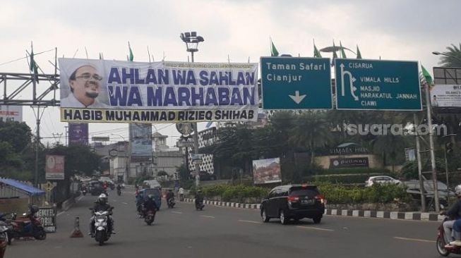 Sebuah spanduk penyambutan kepulangan Habib Rizieq Shihab yang terpasang di plang penunjuk arah di Gadog Ciawi, Bogor, Senin (9/11/2020). [Suara.com/Andi Ahmad Sulaendi]