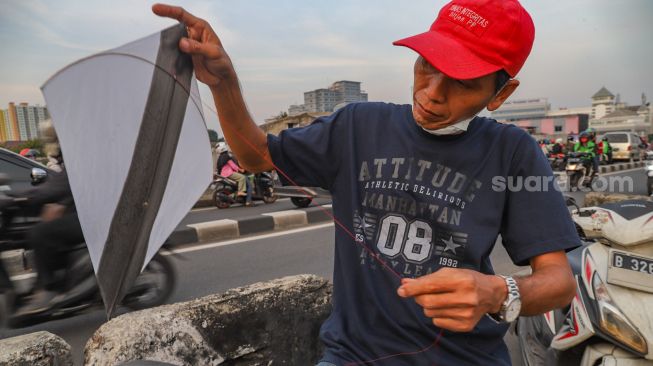 Seorang warga memasang tali di layangannya untuk bermain di samping Fly Over Kalibata, Jakarta Selatan, Senin (9/11). [Suara.com/Alfian Winanto]