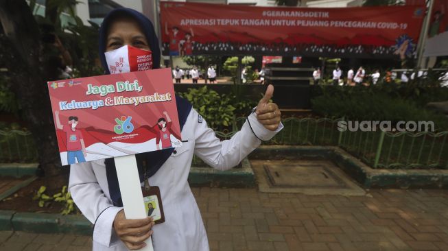 Seorang karyawan Kementerian Kesehatan membawa poster berisi seruan untuk menjaga kesehatan sebelum melakukan tepuk tangan secara bersama di depan Gedung Kementerian Kesehatan Republik Indonesia, Jakarta, Kamis (12/11/2020). [Suara.com/Angga Budhiyanto]