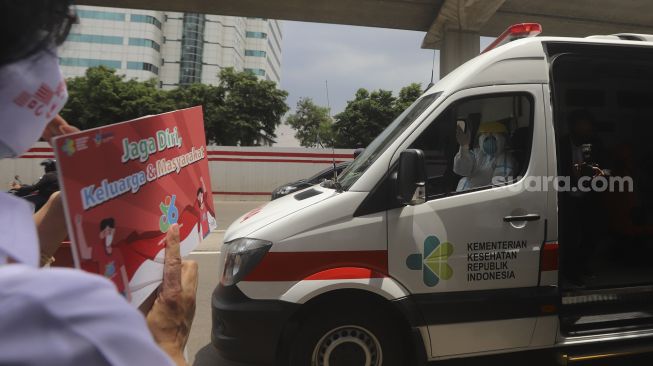 Seorang karyawan Kementerian Kesehatan membawa poster berisi seruan untuk menjaga kesehatan saat 
 melakukan tepuk tangan secara bersama di depan Gedung Kementerian Kesehatan Republik Indonesia, Jakarta, Kamis (12/11/2020). [Suara.com/Angga Budhiyanto]