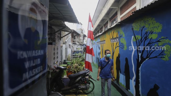 Warga melintas di salah satu gang yang dipenuhi mural di Kampung Sehat, Utan Kayu Selatan, Jakarta, Kamis (12/11/2020). [Suara.com/Angga Budhiyanto]