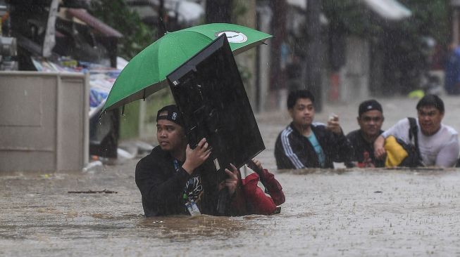 Seorang pria (kiri) membawa televisi saat penduduk melewati jalan yang banjir untuk berlindung di Manila, Filipina, Kamis (12/11/2020).  [Ted ALJIBE / AFP]