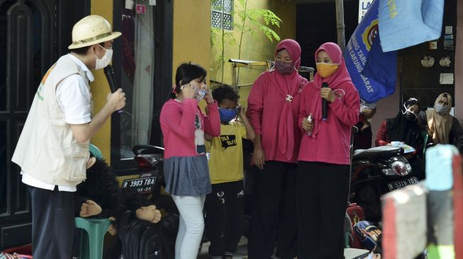 Pendongeng Adi Pamungkas (kiri) memberikan petunjuk bagaimana cara memakai masker yang benar kepada dua orang anak saat mendongeng di hadapan anak-anak warga Cakung Barat, Jakarta Timur, Sabtu (14/11/2020). [ANTARA FOTO/Suwandy]