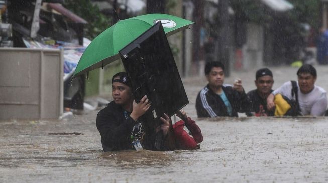 Seorang pria (kiri) membawa televisi saat penduduk melewati jalan yang banjir untuk berlindung di Manila, Filipina, Kamis (12/11/2020).Topan Vamco, topan dahsyat ketiga yang melanda Filipina dalam 11 hari terakhir, mendarat pada Rabu (11/11) malam waktu setempat dengan membawa angin kencang dan hujan deras yang memicu tanah longsor, longsor batu, serta banjir bandang. [Ted ALJIBE / AFP]

