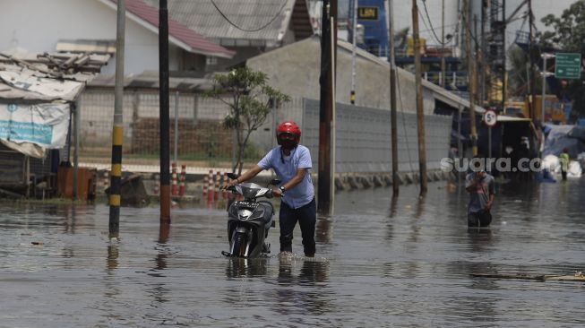 Seorang warga menutun sepeda motornya melintasi banjir rob yang menggenangi kawasan Sunda Kelapa, Jakarta, Selasa (17/11/2020). [Suara.com/Angga Budhiyanto]