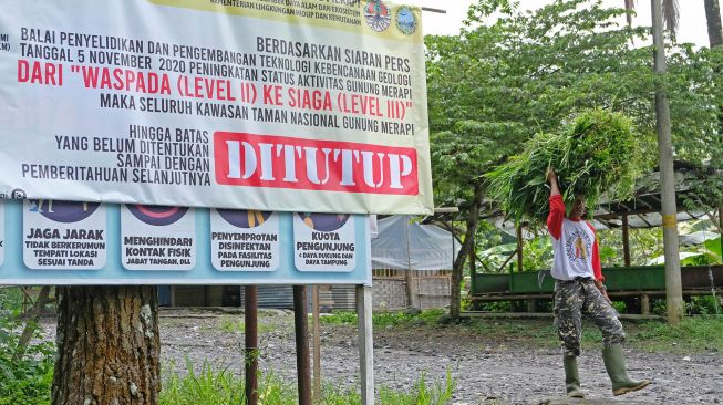 Seorang warga membawa rumput melintasi gerbang Taman Nasional Gunung Merapi Jurang Jero yang ditutup sementara di Ngargosoko, Srumbung, Magelang, Jateng, Rabu (18/11/2020). [ANTARA FOTO/Anis Efizudin]