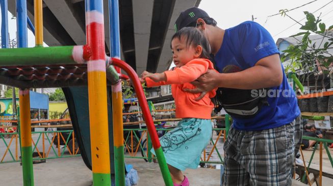 Anak - anak bermain dengan pengawasan orang tua di Taman Bermain yang ada di Kolong Jalan Layang Rawajati, Jakarta Selatan, Kamis (19/11). [Suara.com/Alfian Winanto]