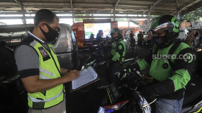 Petugas mencatat hasil uji emisi kendaraan bermotor kepada pengemudi ojek online di Kantor Dinas Lingkungan Hidup DKI Jakarta, Kramat Jati, Jakarta, Kamis (19/11/2020). [Suara.com/Angga Budhiyanto]