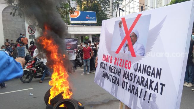 Massa membakar ban bekas dalam aksi demo menolak kedatangan Habib Rizieq di Medan. (Suara.com/Muhlis)