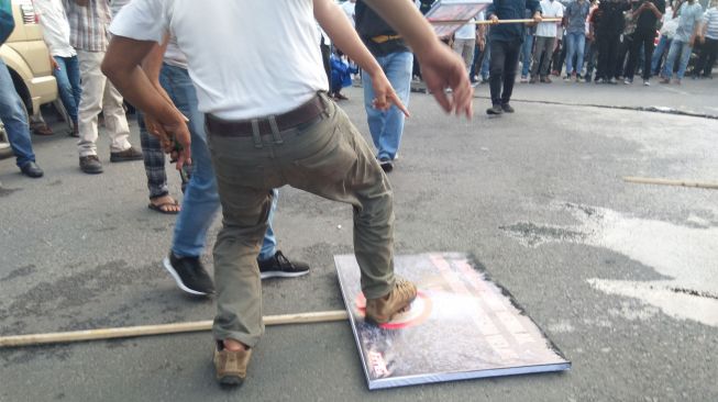 Massa menginjak poster bergambar habib rizieq saat menggelar aksi demo di Medan.  (Suara.com/Muhlis)