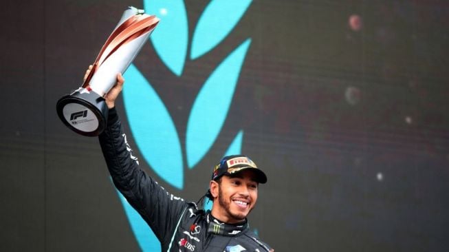 Pebalap Mercedes Lewis Hamilton mengangkat trofi di podium usai memenangi balapan F1 Grand Prix Turki di Istanbul, Minggu (15/11/2020). Pebalap kebanggaan Mercedes, Lewis Hamilton menjuarai F1 GP Turki, sekaligus menyegel gelar juara dunia ketujuhnya. [TOLGA BOZOGLU / POOL / AFP]

