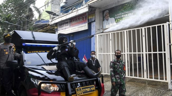 Anggota kepolisian dengan mengenakan hazmat menyemprotkan cairan disinfektan di kawasan Petamburan III, Jakarta Pusat, Minggu (22/11/2020). [ANTARA FOTO/M Risyal Hidayat]