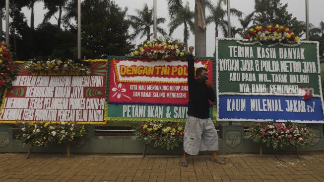 Warga berfoto di depan karangan bunga berisi dukungan terhadap TNI dalam upaya penegakan protokol kesehatan di depan Markas Kodam Jaya, Kramat Jati, Jakarta, Senin (23/11/2020). [Suara.com/Angga Budhiyanto]