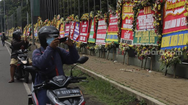 Pengendara sepeda motor berhenti untuk mengabadikan karangan bunga berisi dukungan terhadap TNI dalam upaya penegakan protokol kesehatan di depan Markas Kodam Jaya, Kramat Jati, Jakarta, Senin (23/11/2020). [Suara.com/Angga Budhiyanto]