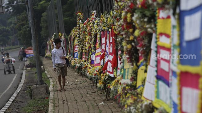 Warga melintas di depan karangan bunga berisi dukungan terhadap TNI dalam upaya penegakan protokol kesehatan di depan Markas Kodam Jaya, Kramat Jati, Jakarta, Senin (23/11/2020). [Suara.com/Angga Budhiyanto]