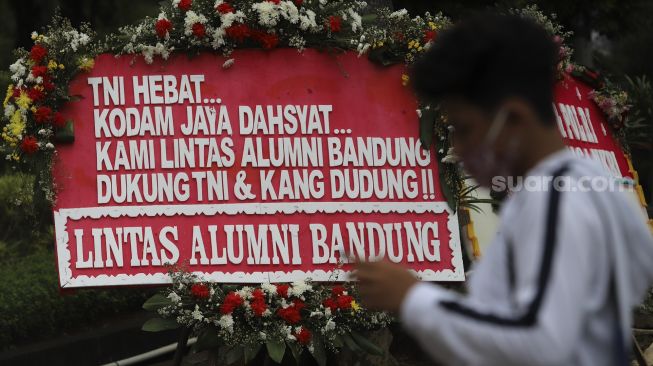 Warga berdiri di depan karangan bunga berisi dukungan terhadap TNI dalam upaya penegakan protokol kesehatan di depan Markas Kodam Jaya, Kramat Jati, Jakarta, Senin (23/11/2020). [Suara.com/Angga Budhiyanto]