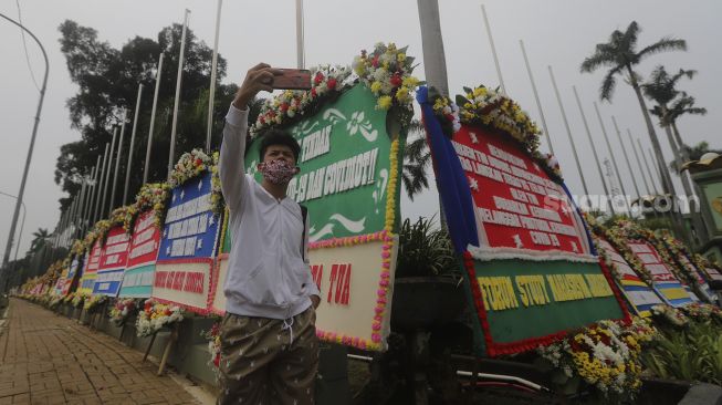 Warga berswafoto di depan karangan bunga berisi dukungan terhadap TNI dalam upaya penegakan protokol kesehatan di depan Markas Kodam Jaya, Kramat Jati, Jakarta, Senin (23/11/2020). [Suara.com/Angga Budhiyanto]