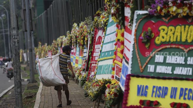 Warga melintas di depan karangan bunga berisi dukungan terhadap TNI dalam upaya penegakan protokol kesehatan di depan Markas Kodam Jaya, Kramat Jati, Jakarta, Senin (23/11/2020). [Suara.com/Angga Budhiyanto]