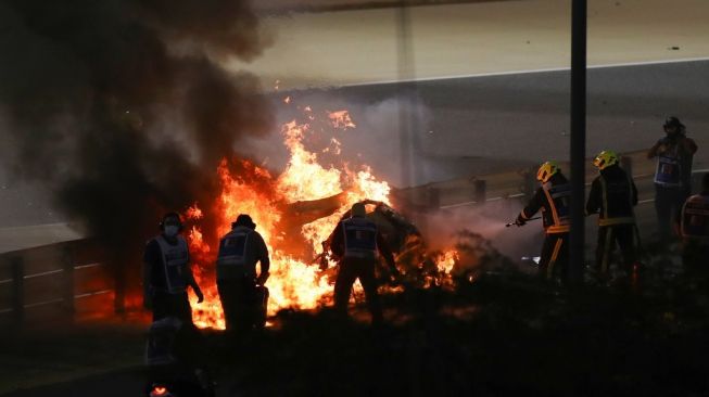 Petugas berusaha memadamkan api di lokasi kecelakaan pembalap Haas, Romain Grosjean pada awal balapan F1 GP Bahrain di Sirkuit Internasional Bahrain, Sakhir, Senin (30/11/2020) dini hari WIB. [BRYN LENNON / POOL / AFP]