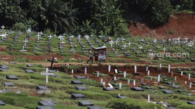 Pedagang melintasi area pemakaman khusus COVID-19 di TPU Pondok Ranggon, Jakarta, Rabu (2/12/2020). [Suara.com/Angga Budhiyanto]