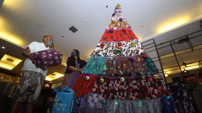 Desainer Embran Nawawi (kiri) menyelesaikan pembuatan pohon Natal berbahan kain batik Pamekasan di Surabaya, Jawa Timur, Kamis (3/12/2020).  [ANTARA FOTO/Moch Asim]