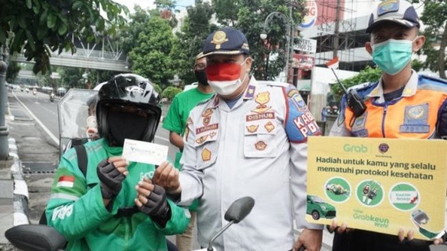 Pejabat Dinas Perhubungan dan perwakilan Grab memberikan hadiah kepada warga warga yang taat protokol kesehatan di Kota Bandung, Jawa Barat [HO Humas Grab]via ANTARA].