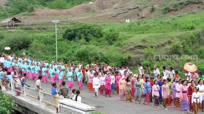 Upacara adat pernikahan khas Lombok, saat pengantin (lelaki di belakang dan perempuan jauh di depan, lihat posisi payung) diarak di ruas jalan raya. Diabadikan jauh sebelum pandemi COVID-19 yang memiliki prokes tidak menciptakan kerumunan [Suara.com/CNR ukirsari].