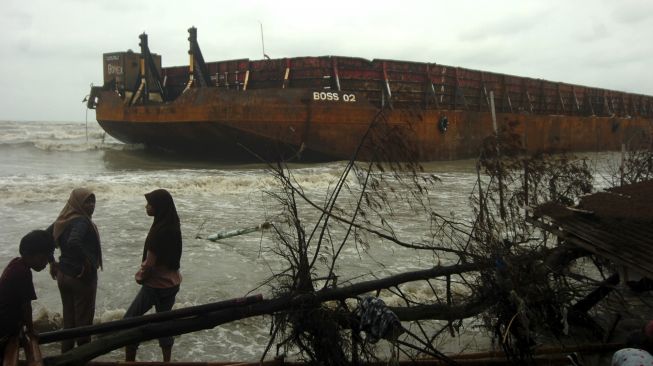 Sejumlah warga berdiri di samping kapal Tongkang yang terdampar, di Pantai Utara, Martoloyo, Tegal, Jawa Tengah, Senin (7/12/2020). [ANTARA FOTO/Oky Lukmansyah]