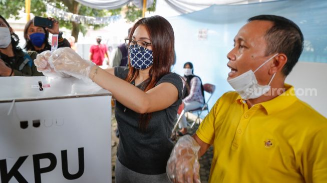 Pedangdut Ayu Ting Ting bersama sang ayah, Abdul Rozak memasukkan surat suaranya kedalam kotak suara saat melakukan pemilihan kepala daerah di TPS 06 Sukmajaya, Depok, Jawa Barat, Rabu (9/12). [Suara.com/Alfian Winanto]