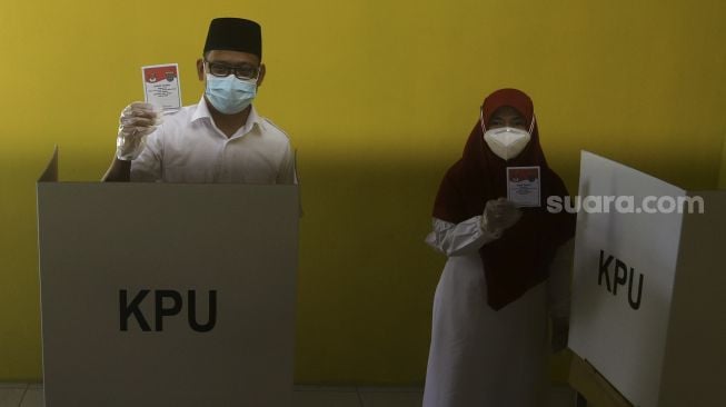 Calon Wakil Wali Kota Depok Imam Budi Hartono didampingi istrinya Etty Maryati Salim menunjukkan surat suara sebelum menggunakan hak pilih dalam Pilkada Depok di TPS 47, Kompleks Acacia, Grand Depok City, Depok, Jawa Barat, Rabu (9/12/2020). [Suara.com/Angga Budhiyanto]