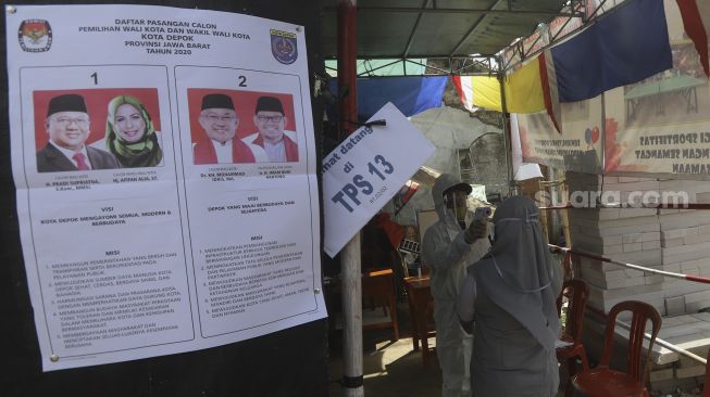 Petugas KPPS mengenakan pakaian hazmat dan Alat Perlindungan Diri (APD) memindai suhu tubuh warga yang akan menggunakan hak pilihnya di Tempat Pemungutan Suara (TPS) 13 Pasir Putih, Sawangan, Depok, Jawa Barat, Rabu (9/12/2020). [Suara.com/Angga Budhiyanto]