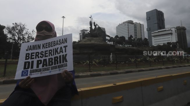 Seorang massa buruh membawa poster saat melakukan aksi unjuk rasa di kawasan Patung Kuda Arjuna Wiwaha, Jakarta, Kamis (10/12/2020). [Suara.com/Angga Budhiyanto]