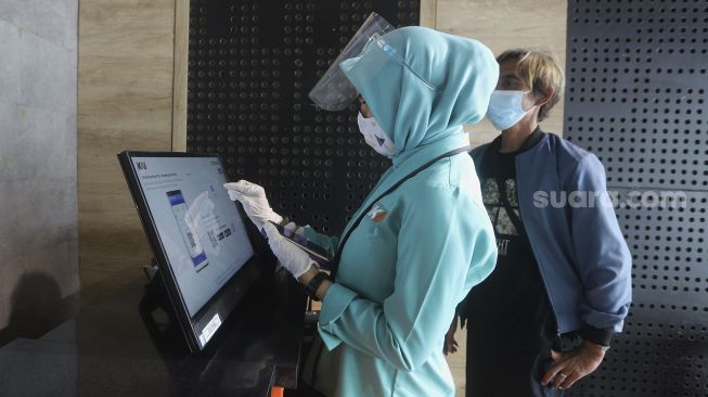 Petugas membantu calon penumpang mencetak tiket di Stasiun Pasar Senen, Jakarta, Kamis(10/12/2020). [Suara.com/Angga Budhiyanto]