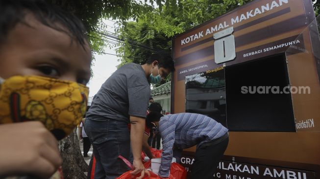 Seorang anak mengantre untuk mengambil makanan gratis di Kotak Amal Makanan Gratis di pelataran Masjid Cut Meutia, Jakarta, Jumat (11//12/2020). [Suara.com/Angga Budhiyanto]