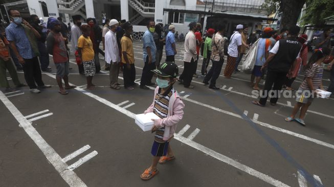 Seorang anak bergegas usai mengambil makanan gratis di Kotak Amal Makanan Gratis di pelataran Masjid Cut Meutia, Jakarta, Jumat (11//12/2020). [Suara.com/Angga Budhiyanto]