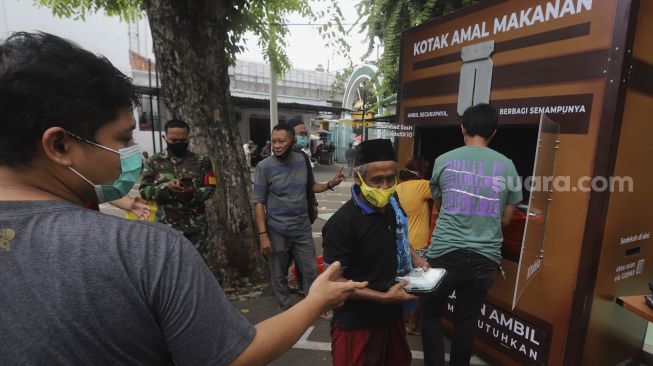 Warga mengambil makanan gratis di Kotak Amal Makanan Gratis di pelataran Masjid Cut Meutia, Jakarta, Jumat (11//12/2020). [Suara.com/Angga Budhiyanto]