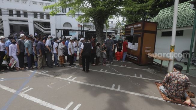 Sejumlah warga mengantre untuk mengambil makanan gratis di Kotak Amal Makanan Gratis di pelataran Masjid Cut Meutia, Jakarta, Jumat (11//12/2020). [Suara.com/Angga Budhiyanto]